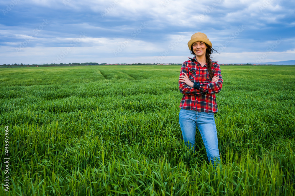 Satisfied female farmer is standing in her barley field.