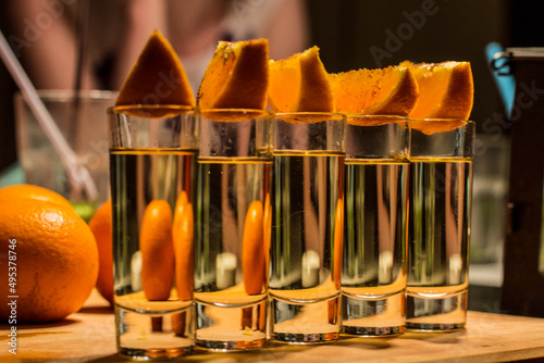 Becherovka in small glasses on a wooden background with oranges on the top and behind photo