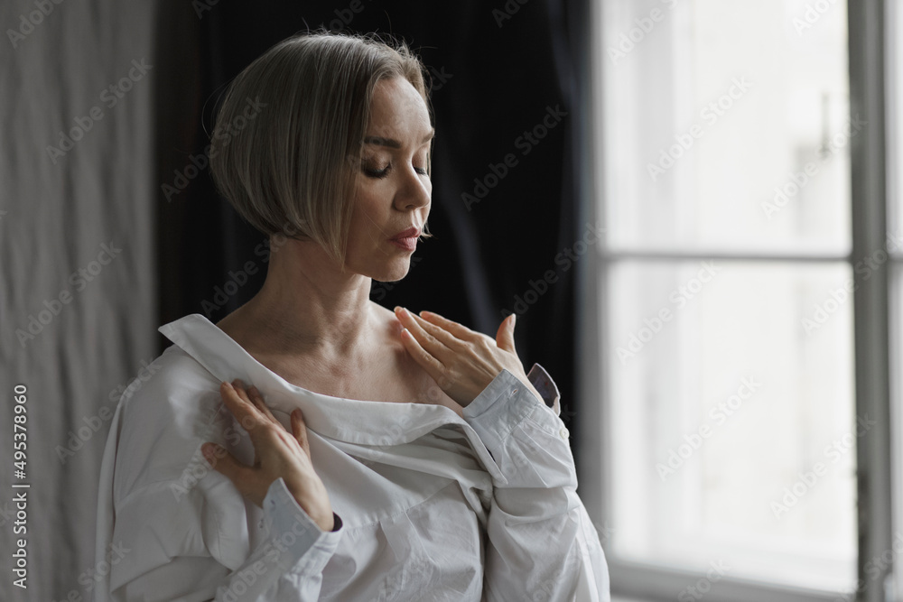Woman with unbuttoned shirt standing in front of window at home Woman with unbuttoned shirt standing in front of window at home