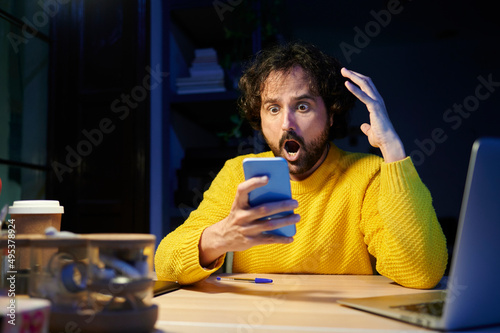 Shocked businessman holding mobile phone sitting at desk in office