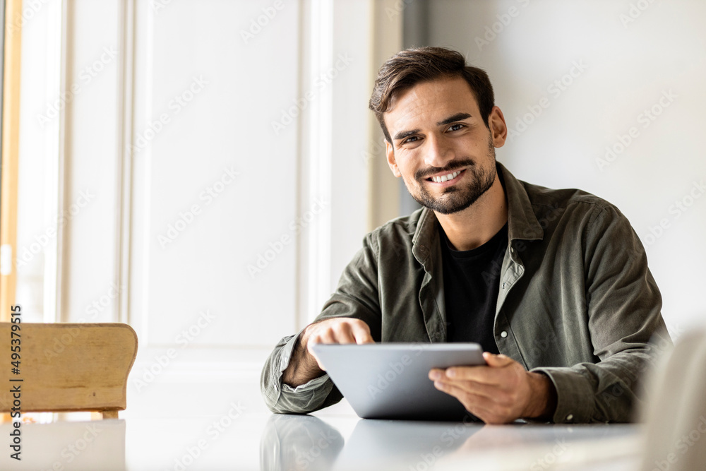 Smiling man sitting at table with tablet PC at home Smiling man sitting at table with tablet PC at home