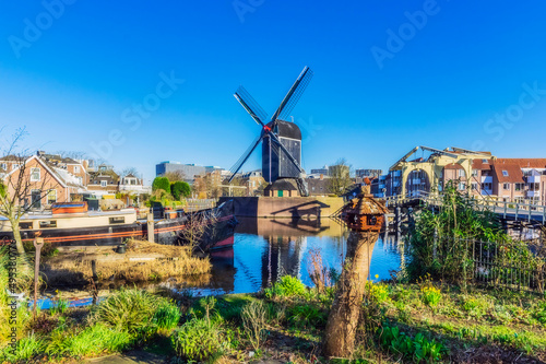 Netherlands, South Holland, Leiden, Clear blue sky over city canal with traditional windmill in background photo