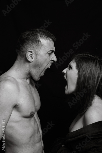 A black and white vertical image of a man and a woman who appear to be having a loud argument. Bare-chested man yelling at a woman who is also yelling.