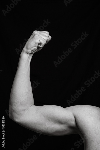 Vertical black and white image of an arm arm closed by the biceps making force. Close shot of a man's arm with their elbow and fingers closed together leaving copy space.