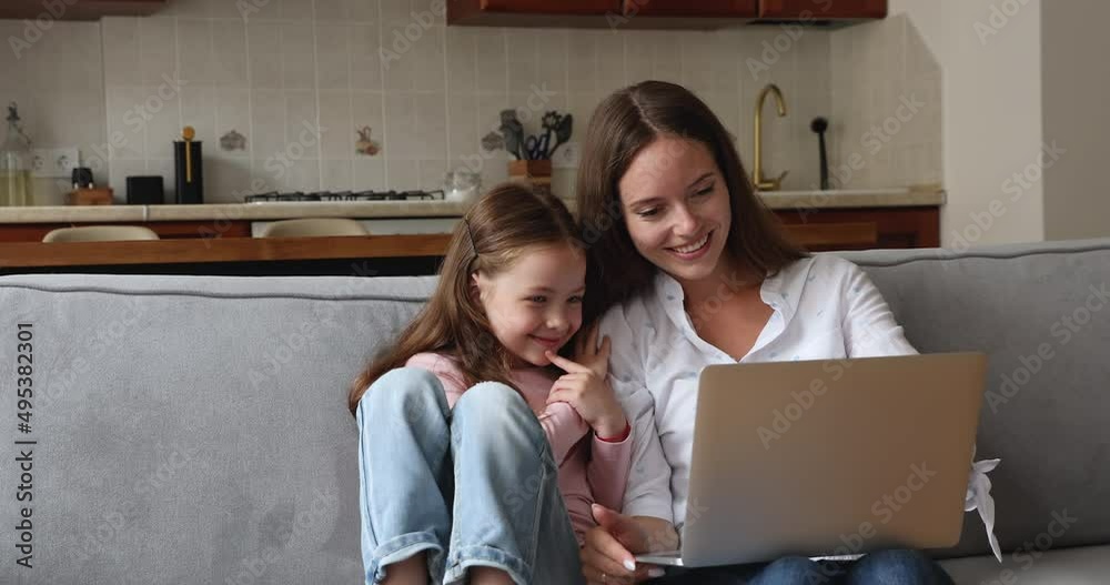 Young woman and preschool 6s daughter make easy comfort purchase use laptop, rest on sofa enjoy free time on internet, mom teach kid use device, have fun buy goods and services in web store concept Young woman and preschool 6s daughter make easy comfort purchase use laptop, rest on sofa enjoy free time on internet, mom teach kid use device, have fun buy goods and services in web store concept