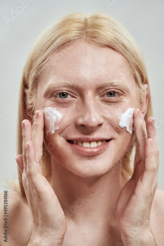 Portrait of guy smearing cosmetic cream on face
