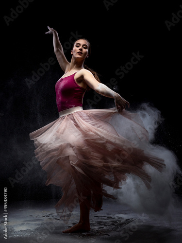 Chica joven bailando en movimiento con polvos de harina en dispersión con fondo oscuro. 
Baile y danza artística. 