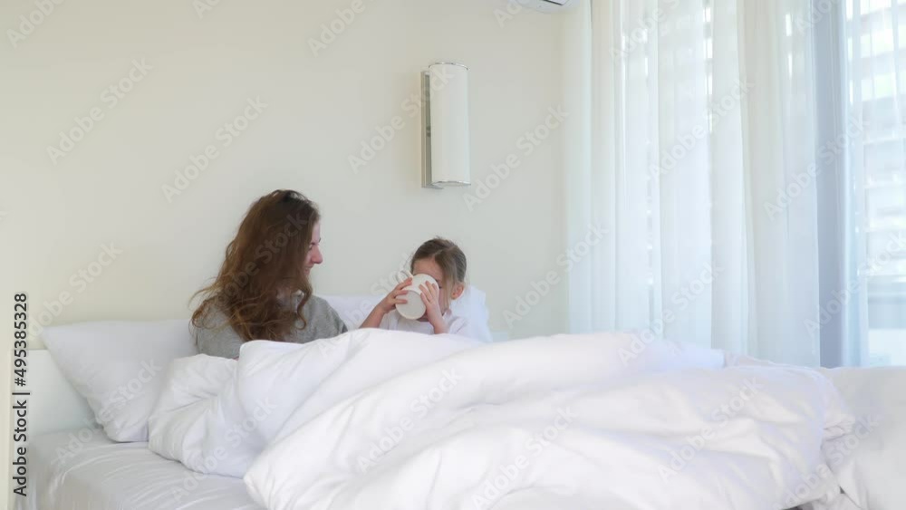 daughter went to bed with her mother. happy and cheerful family concept. child plays with woman. sisters drink coffee from cup. A mug of tea in bed in hotel. Morning in bedroom. Have fun together. daughter went to bed with her mother. happy and cheerful family concept. child plays with woman. sisters drink coffee from cup. A mug of tea in bed in hotel. Morning in bedroom. Have fun together.