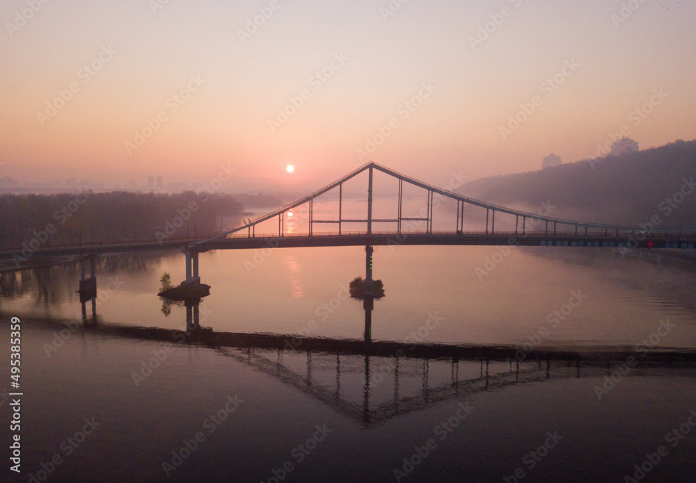 Kyiv, Ukraine - 04 MAY 2021: Aerial view of a pedestrian iron bridge across the Dnepr in Kyiv. Sunrise on the background of the silhouette of the bridge. The peaceful sky over Kyiv.
