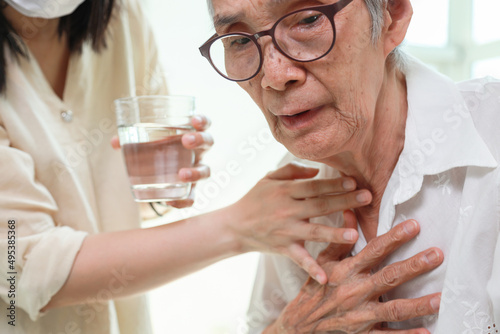 Asian senior woman coughing choking while drinking water or eating food,danger or risk of lung infection,disease of silent aspiration pneumonia,old elderly patient choking water after taking the pills photo
