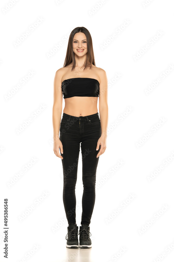 Front view of a young smiling woman in black jeans and short top posing on a white background Front view of a young smiling woman in black jeans and short top posing on a white background