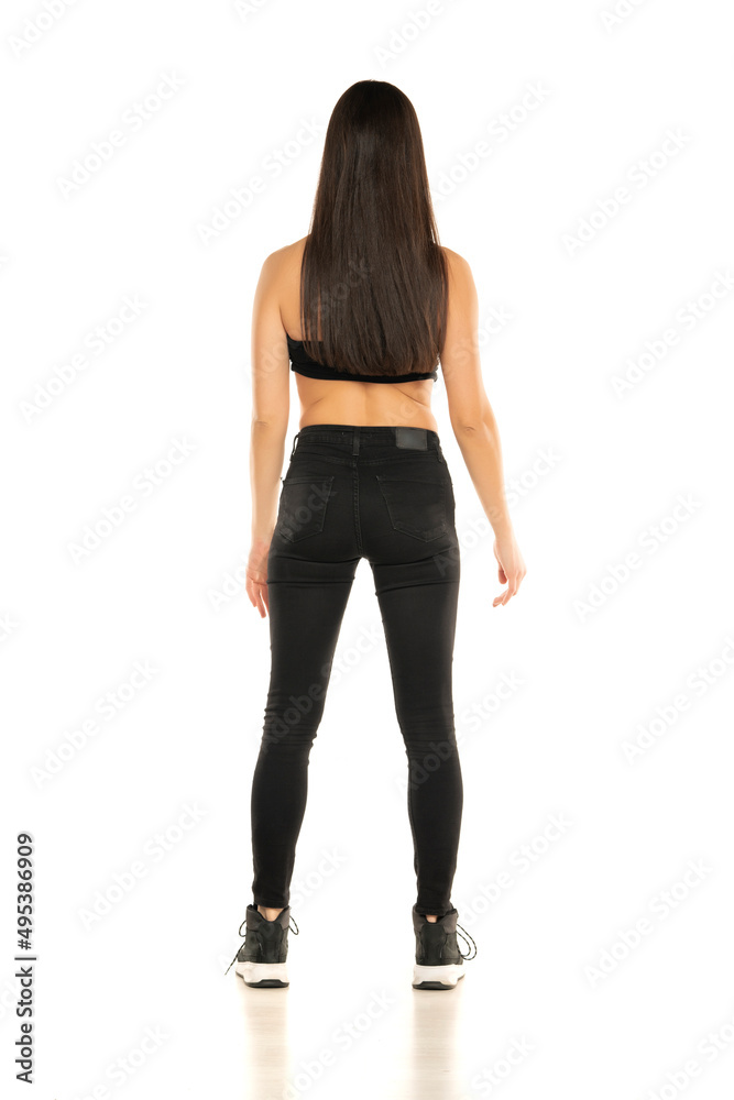 Rear view of a young woman in black jeans and short top posing on a white background Rear view of a young woman in black jeans and short top posing on a white background