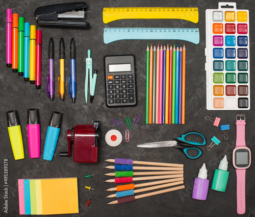 School supplies and child’s smart watches on black background flat lay. Colorful stationery top view.