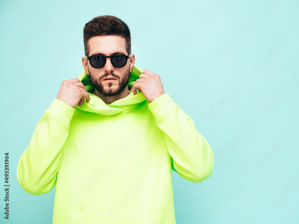 Portrait of handsome smiling model. Sexy stylish man dressed in yellow hoodie with no logo. Clothes branding mockup. Design template for casual sportswear. Fashion male isolated on blue in studio Portrait of handsome smiling model. Sexy stylish man dressed in yellow hoodie with no logo. Clothes branding mockup. Design template for casual sportswear. Fashion male isolated on blue in studio