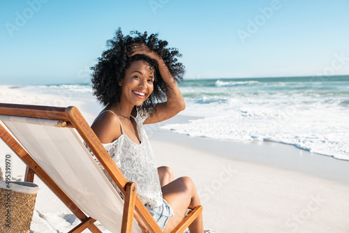 Happy smiling young woman sitting on deck chair at beach during summer vacation