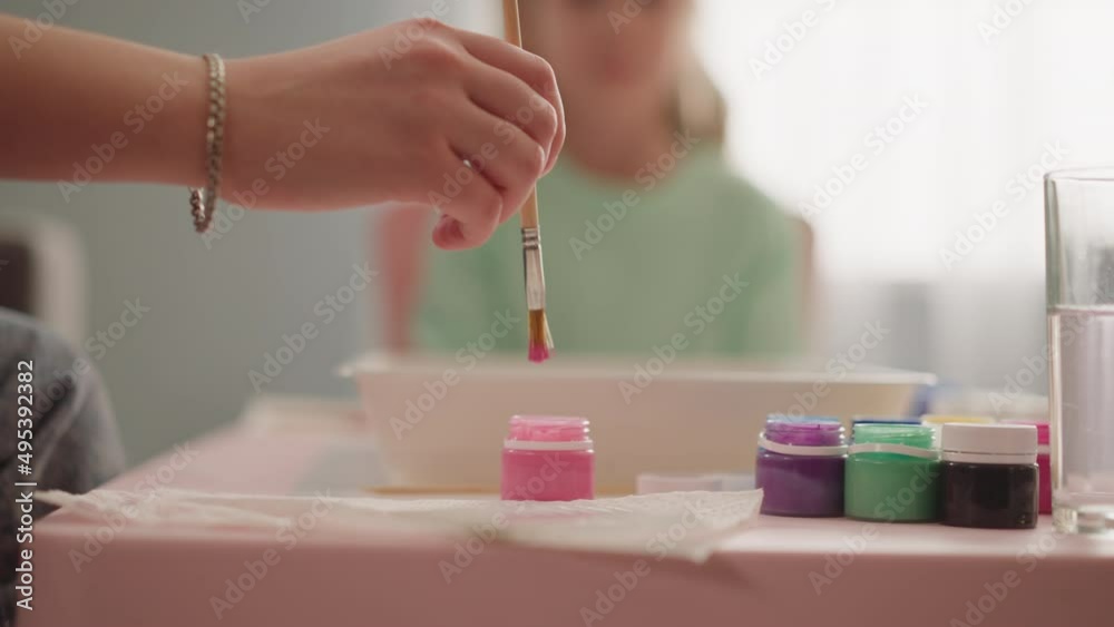 Lady takes pink paint with brush to show little girl Ebru drawing technique in classroom closeup slow motion. Conducting art lesson for child