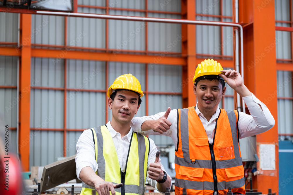 Selective focus at Asian men mechanical engineer, wearing safety equipment. While doing machine maintenance and safety control inside of factory area. With blurred background of heavy machine. Selective focus at Asian men mechanical engineer, wearing safety equipment. While doing machine maintenance and safety control inside of factory area. With blurred background of heavy machine.