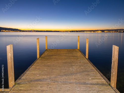 View onto horizon after the sunset on winter day in december with wooden pier in the foreground and city with light at the horizon
