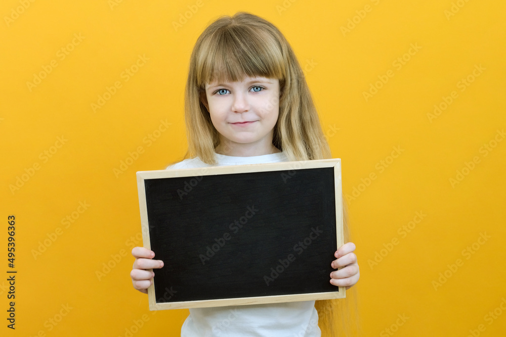 girl holding a board sheet. Cute little girl with chalk board. yellow background. copy space.
