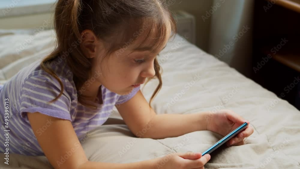 Child is lying on the bed in bedroom with a gadget. Child is lying on the bed in bedroom with a gadget.