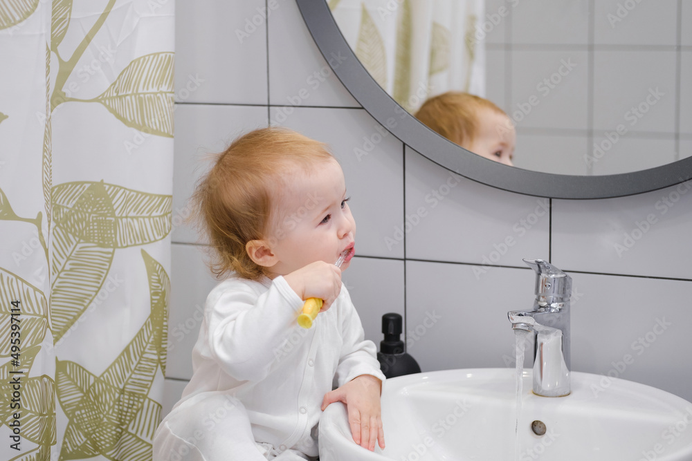 A toddler sitting on the washbasin cabinet and brushing teeth, showing independence, learning new skills. Daily morning hygiene routine. Personal and teeth hygiene. A toddler sitting on the washbasin cabinet and brushing teeth, showing independence, learning new skills. Daily morning hygiene routine. Personal and teeth hygiene.