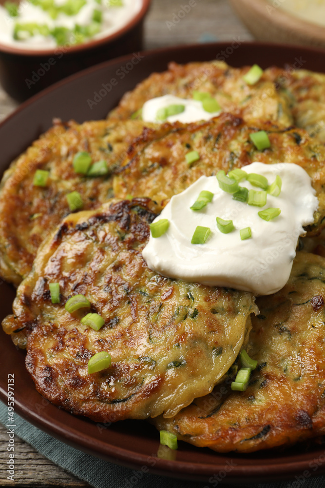 Delicious zucchini pancakes with sour cream and green onion on table, closeup Delicious zucchini pancakes with sour cream and green onion on table, closeup