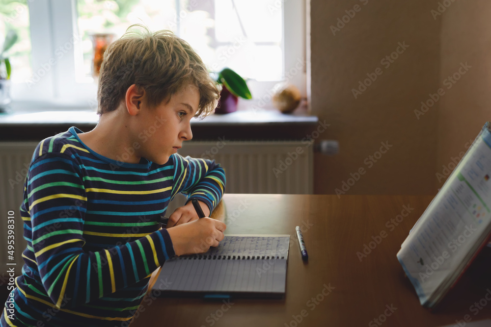 Hard-working school kid boy making homework during quarantine time from corona pandemic disease. Child on home schooling in coronavirus covid time, schools closed. Homeschooling concept - obrazy, fototapety, plakaty 