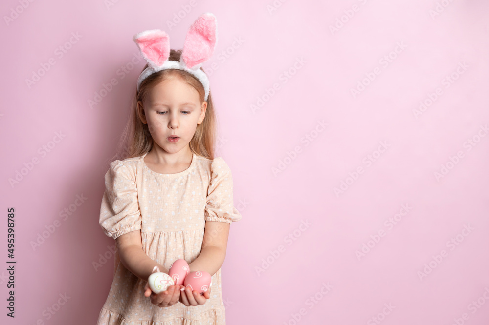 Happy Easter. A cute girl with rabbit ears holds colored eggs in her hands and smiles cheerfully. pink background. Space for text. Happy Easter. A cute girl with rabbit ears holds colored eggs in her hands and smiles cheerfully. pink background. Space for text.