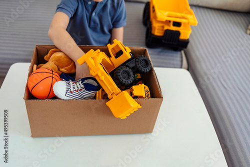 Boy preparing cardboard donation box full with toys. Concept of volunteering work, donation and clothes recycling. Helping poor people. Boy holding card box with his old toys inside. Donation concept.