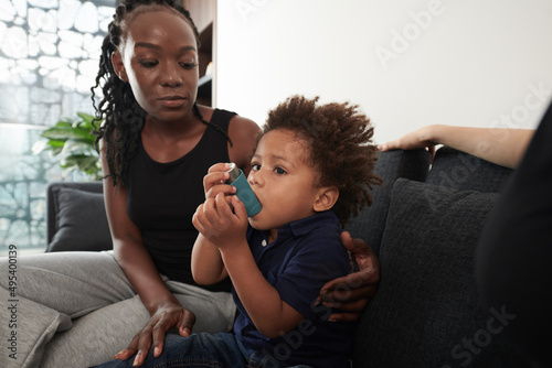 Worried mother looking at son using inhaler when having asthma attack at home photo
