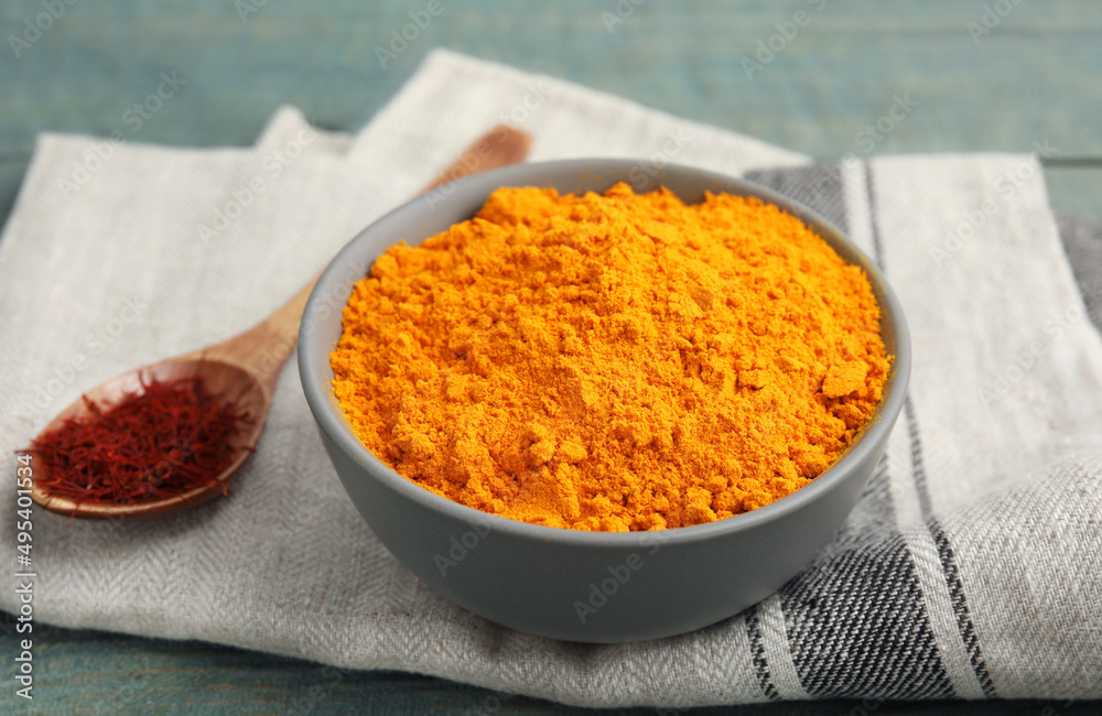 Bowl of saffron powder and spoon with dried flower stigmas on light blue wooden table Bowl of saffron powder and spoon with dried flower stigmas on light blue wooden table