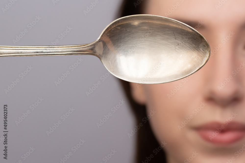 Closeup of a woman using a cold spoon to depuff her undereye area in the morning.