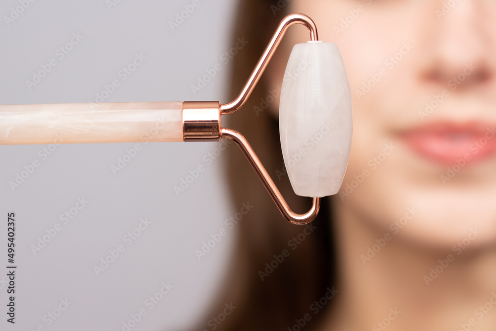 Closeup of a woman using a rose quartz roller to depuff her face in the morning.