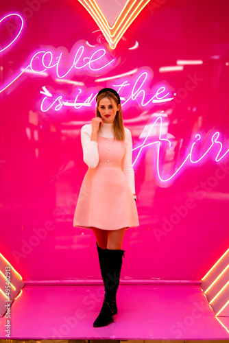 Portrait of attractive, beautiful, caucasian, positive girl in cocktail dress, holding the bottom of her dress with one hand, standing over pink background