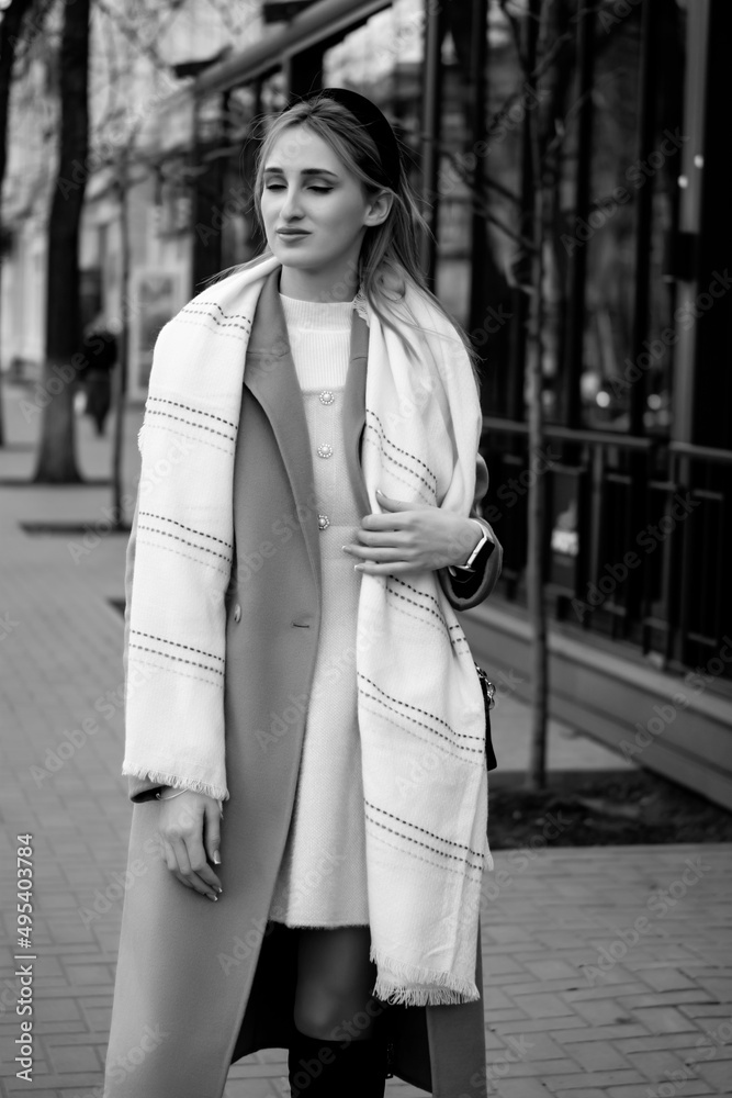 Joyful young woman in oversized checkered coat, sunglasses and beige hat smiles widely and walks around city. Joyful young woman in oversized checkered coat, sunglasses and beige hat smiles widely and walks around city.
