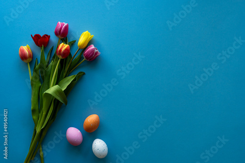Stylish background with colorful easter eggs isolated on blue background with colorful tulip flowers. Flat lay, top view, mockup, overhead, template