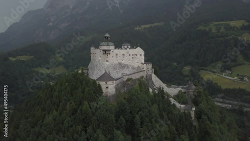 Aerial orbit of medieval Hohenwerfen Fortress on top of a steep hill, surrounded by pine forest and Berchtesgaden Alps in Werfen, Salzburg, Austria photo