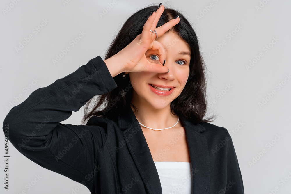 Face portrait of beautiful teen girl smiling, showing okay, ok, zero no problem gesture and laughing, wearing in black blazer, standing over grey background. Young emotional woman Face portrait of beautiful teen girl smiling, showing okay, ok, zero no problem gesture and laughing, wearing in black blazer, standing over grey background. Young emotional woman