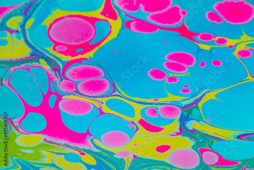 Colorful background with pink, blue and yellow marble spots in Turkish ebru technique. Unique artistic marble texture background, drawing with acrylic paints on the surface of the water. Close up.