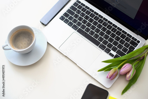 Home office desk with laptop, smartphone, pink tulips and cup of coffee on white table. Flat lay Business workplace. Top view. Laptop for businesswoman 