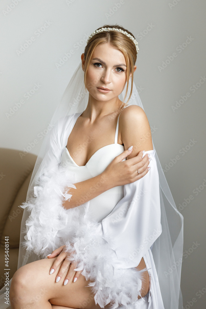 Gorgeous beautiful bride in silk robe posing near window in soft light in the morning. Gorgeous beautiful bride in silk robe posing near window in soft light in the morning.