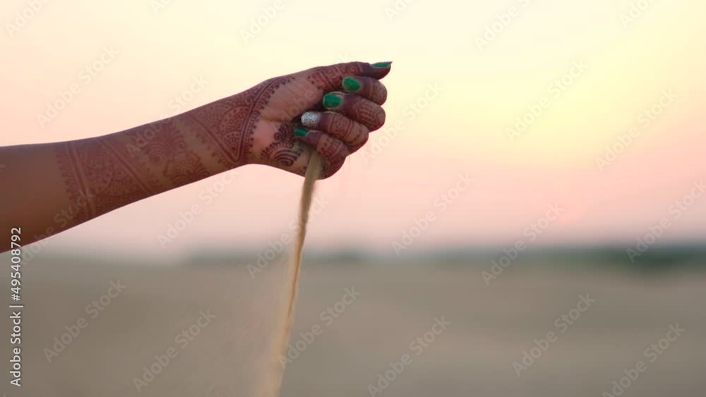 Slow motion shot of hands of an Indian female pouring sand of the Thar desert at Sam Sand dunes in Jaisalmer, Rajasthan, India. Female pouring sand in the desert. Desert Travel background.	