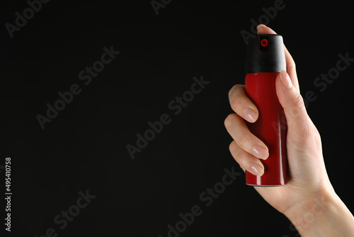 Woman holding pepper spray on black background, closeup. Space for text photo