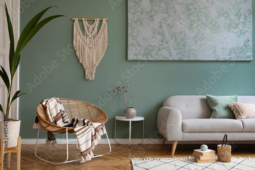 Creative living room interior design composition with crey scandi sofa, rattan armchair, plants, carpet and beautiful boho accessories. Eucalyptus walls and parquet floor. photo