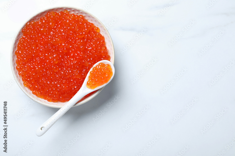 Bowl and spoon with delicious red caviar on white table, top view. Space for text Bowl and spoon with delicious red caviar on white table, top view. Space for text