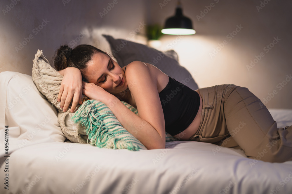 Naklejka premium Chica joven delgada tumbada de lado sobre cama de hotel mientras descansa y mira el smartphone