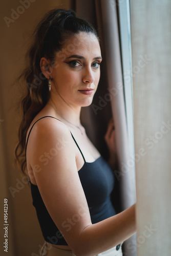 Fotografie Chica joven delgada abriendo cortina en habitación de hotel
