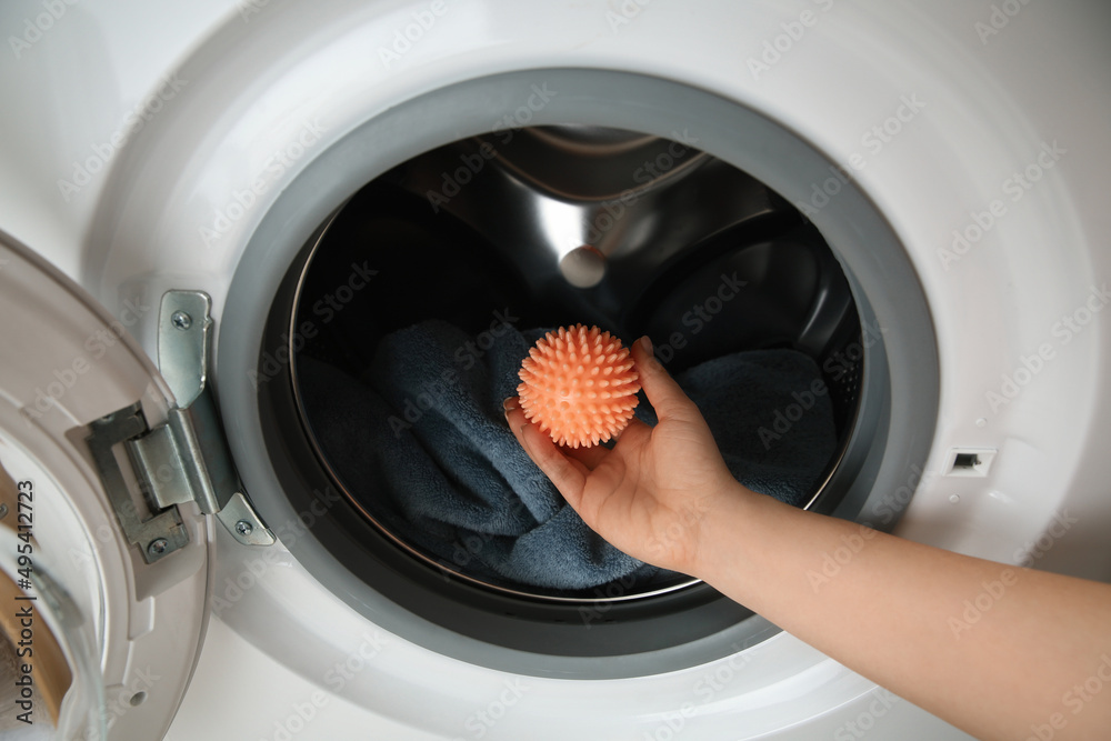 Woman putting dryer ball into washing machine, closeup