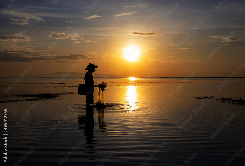 Silhouette Balinese male fishing Indonesian coastline at sunrise