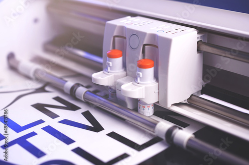 cutting plotter machine with adjustable blades makes adhesive lettering from black vinyl foil in bright light with blue highlights. selective focus. advertising concept